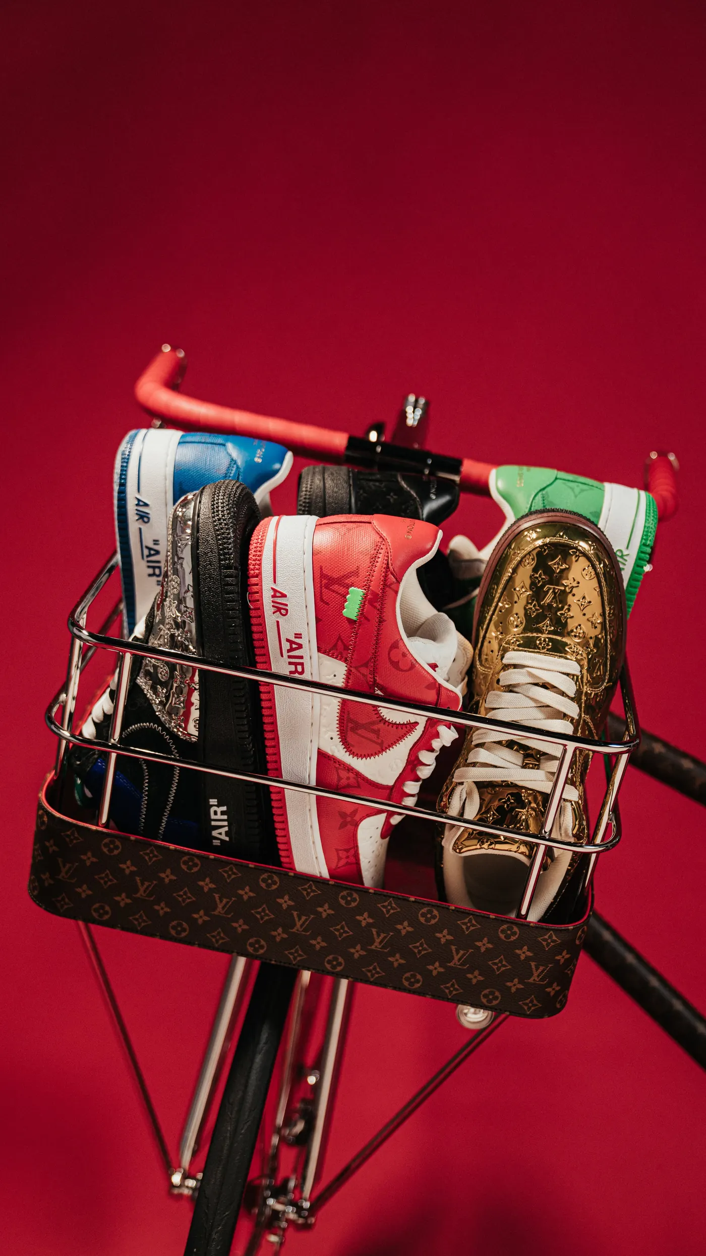 Canasta de bicicleta llena de tenis Nike y Louis Vuitton sobre fondo rojo